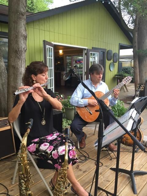 Two musicians playing flute and guitar on an outdoor deck